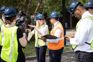 Maurie McInnis and other people are wearing a hard hats with equipment visible in the background.